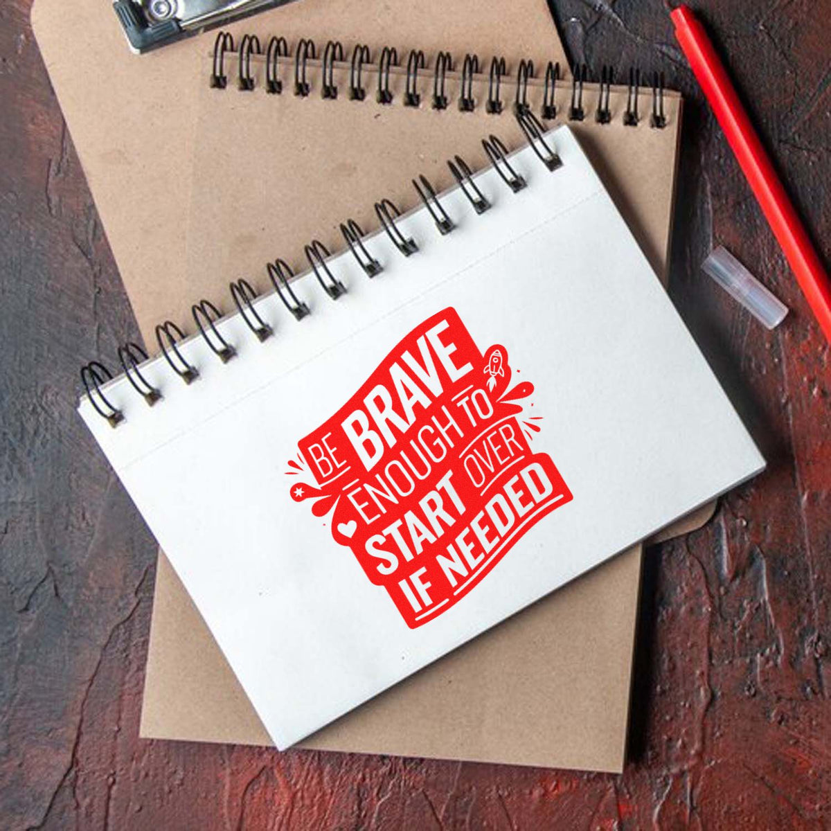 Motivational rubber stamp design reading Be brave enough to start over if needed on a spiral notebook.