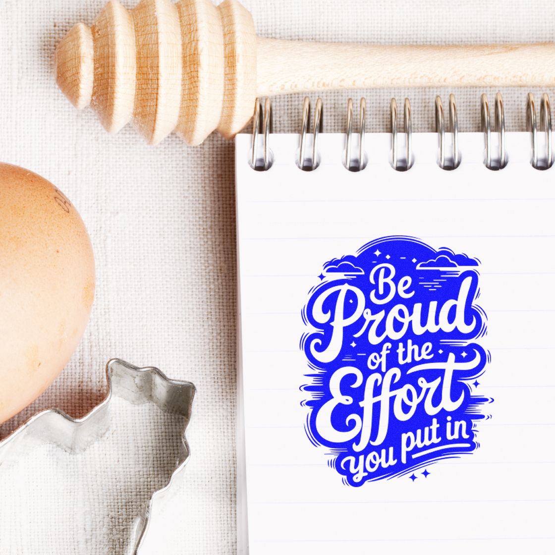 Blue rubber stamp-style quote reading Be Proud of the Effort You Put In on a notebook, ideal for motivational crafting and journaling.