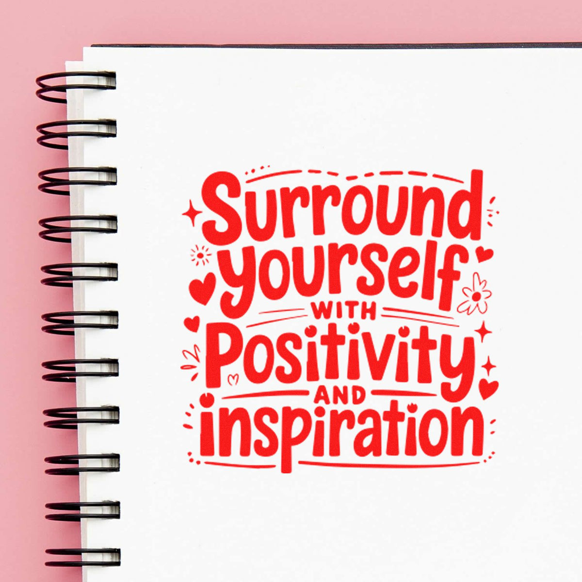 Red rubber stamp design reading Surround yourself with positivity and inspiration on a spiral notebook page.