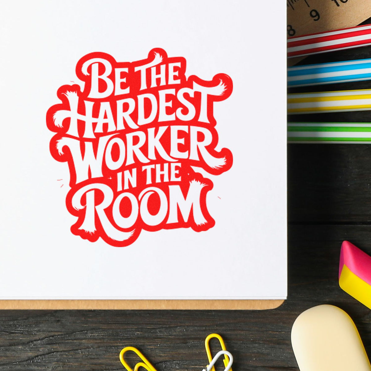 Motivational rubber stamp reading Be the Hardest Worker in the Room in bold red on white paper, ideal for office branding.