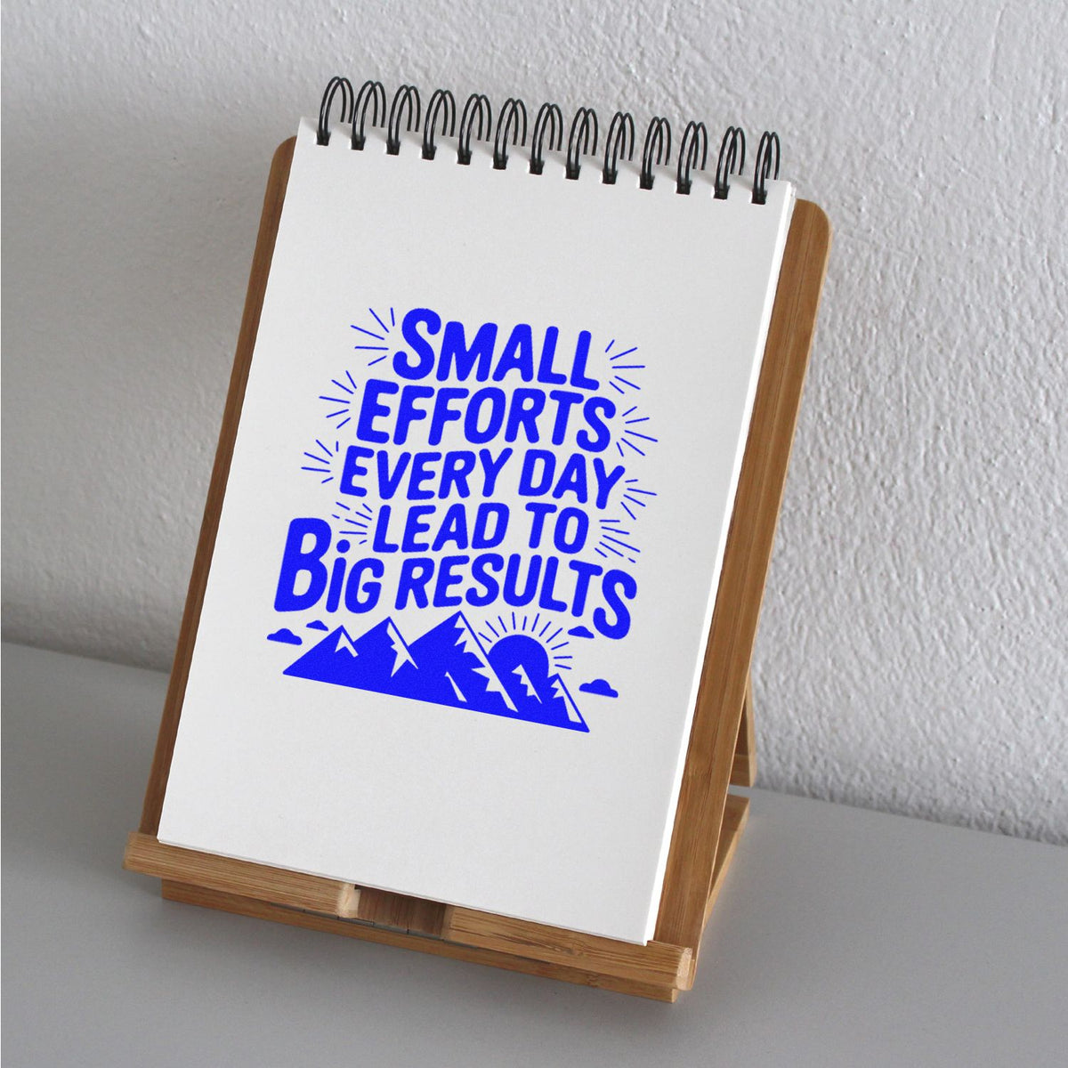 Motivational rubber stamp impression reading Small efforts every day lead to big results on a notebook display.