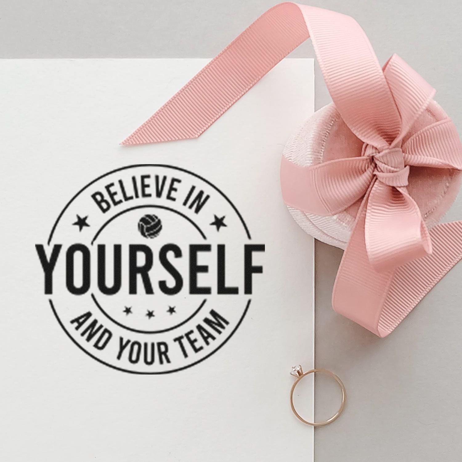 Motivational rubber stamp reading Believe in Yourself and Your Team on gift packaging with a pink ribbon bow.