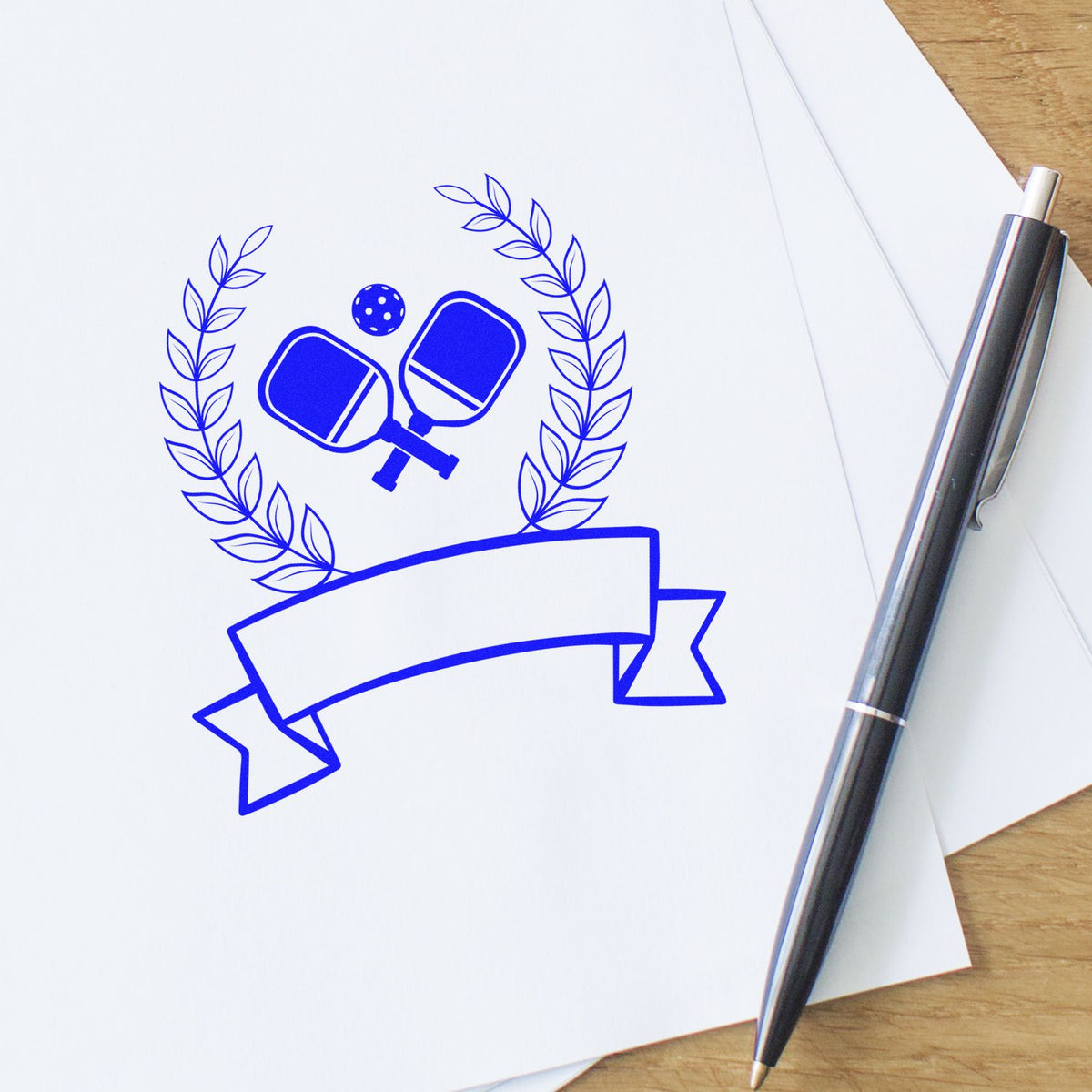Custom rubber stamp of ping pong paddles with laurel and banner printed on paper beside a pen