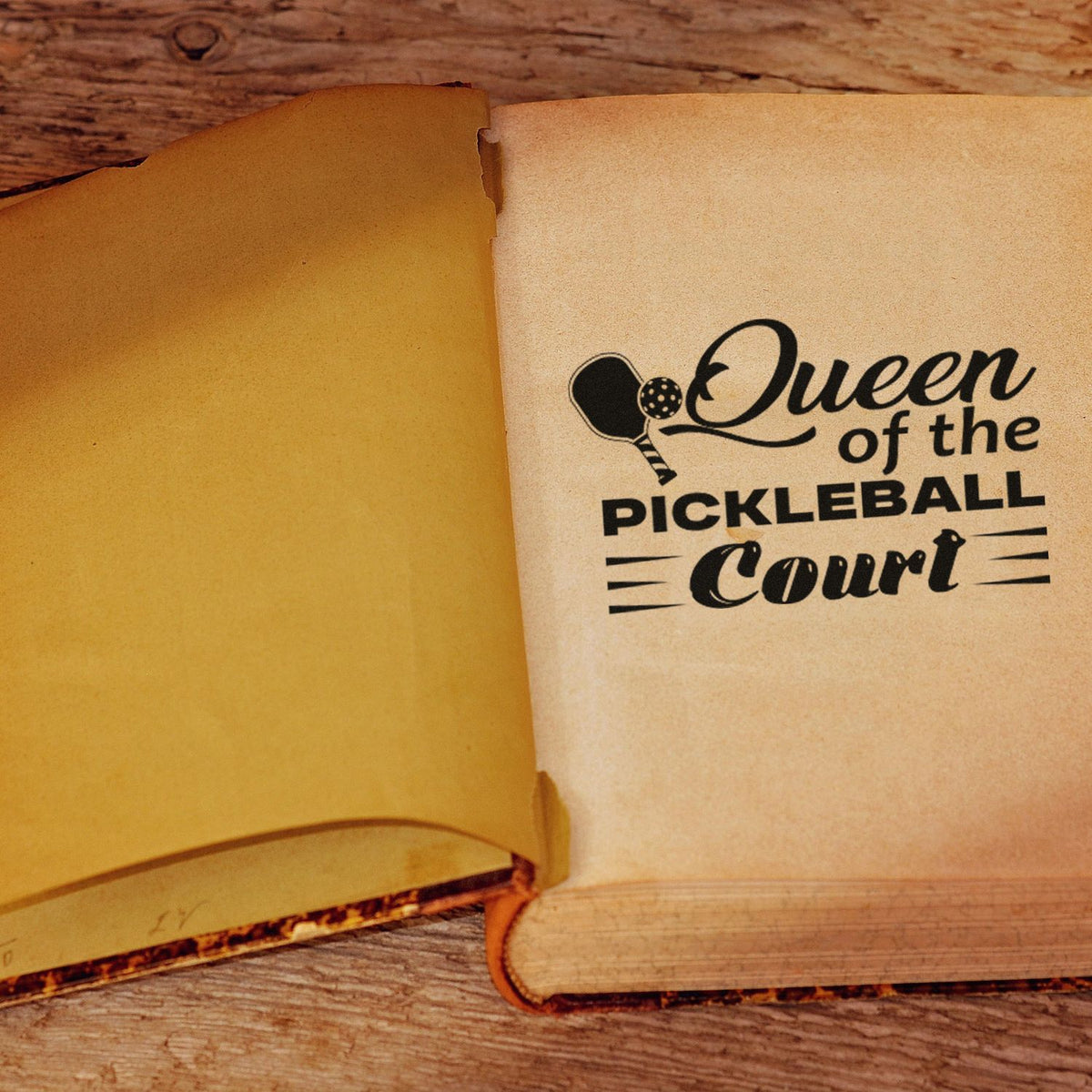 Custom rubber stamp reading Queen of the Pickleball Court on an open book page, ideal for pickleball fans.