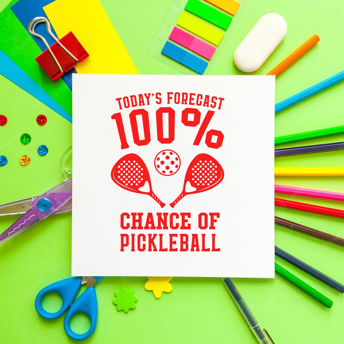 100% Chance of Pickleball rubber stamp design with paddles and ball on a colorful craft supplies background.