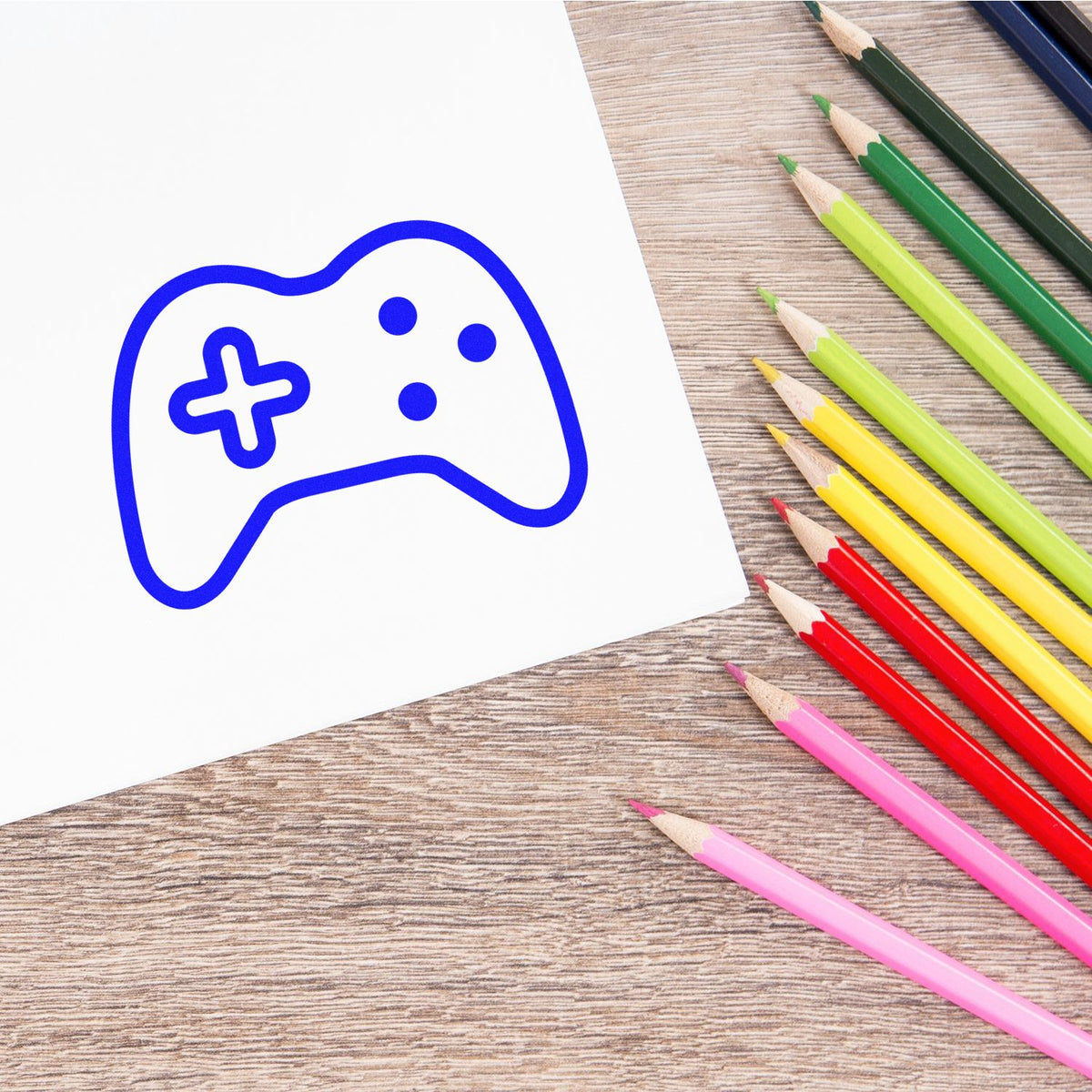 Blue game controller rubber stamp design on paper with colored pencils, ideal for custom gaming-themed stamps.