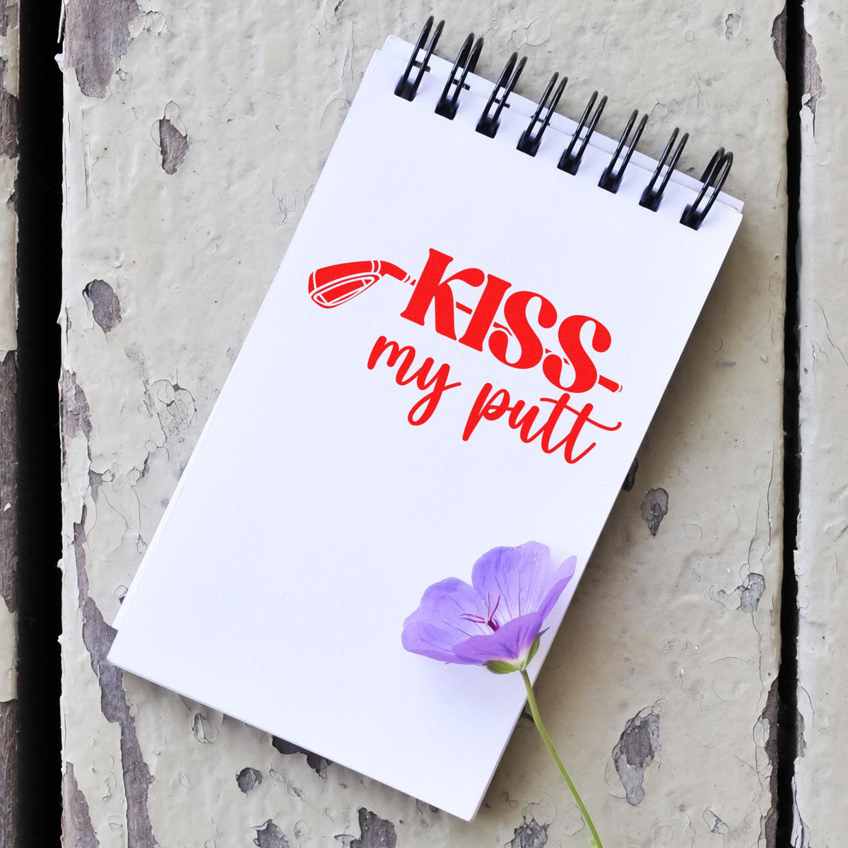 Custom rubber stamp design reading Kiss My Putt for golf crafts, shown on a white spiral notebook.