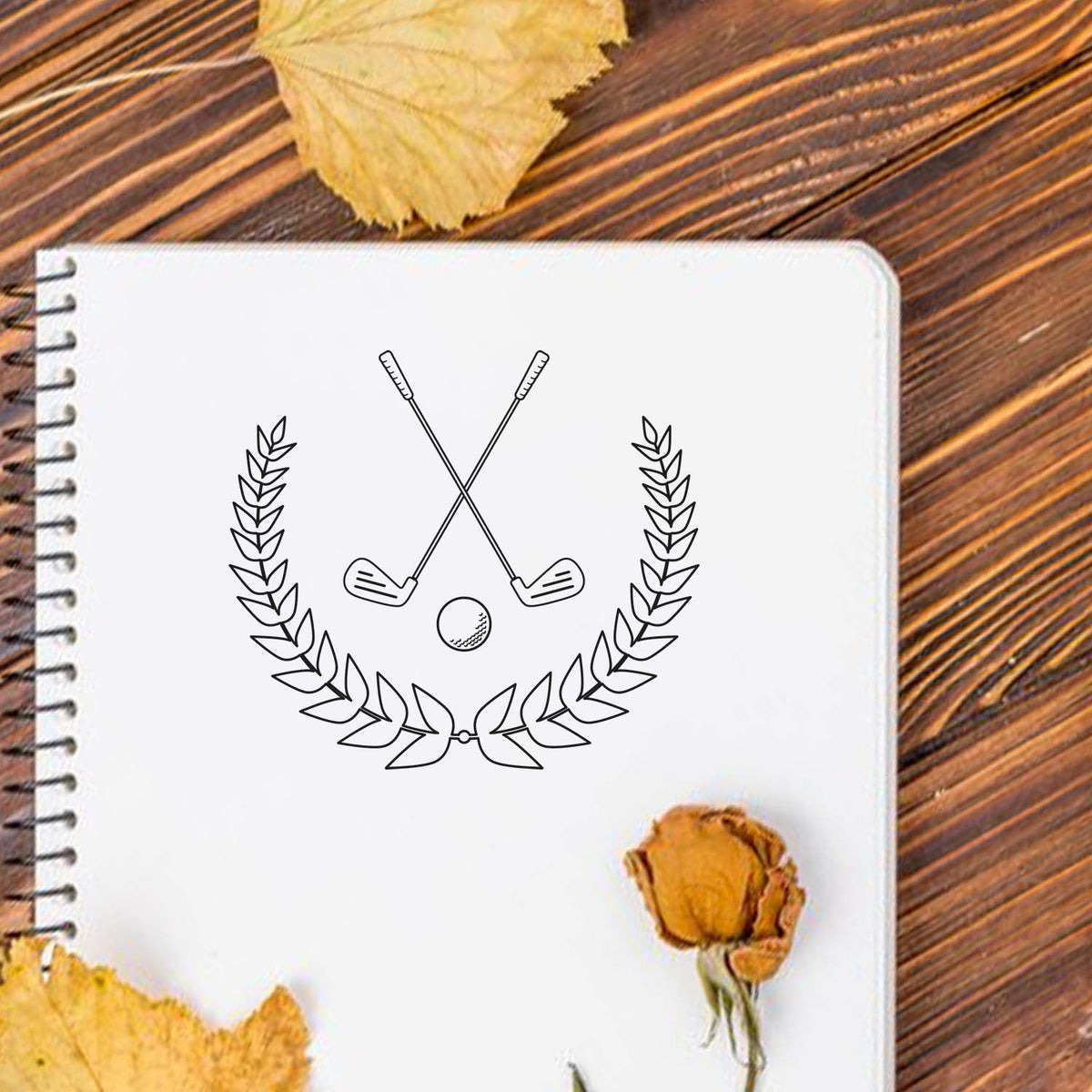 Golf club rubber stamp design with crossed golf clubs, laurel wreath, and golf ball logo on notebook