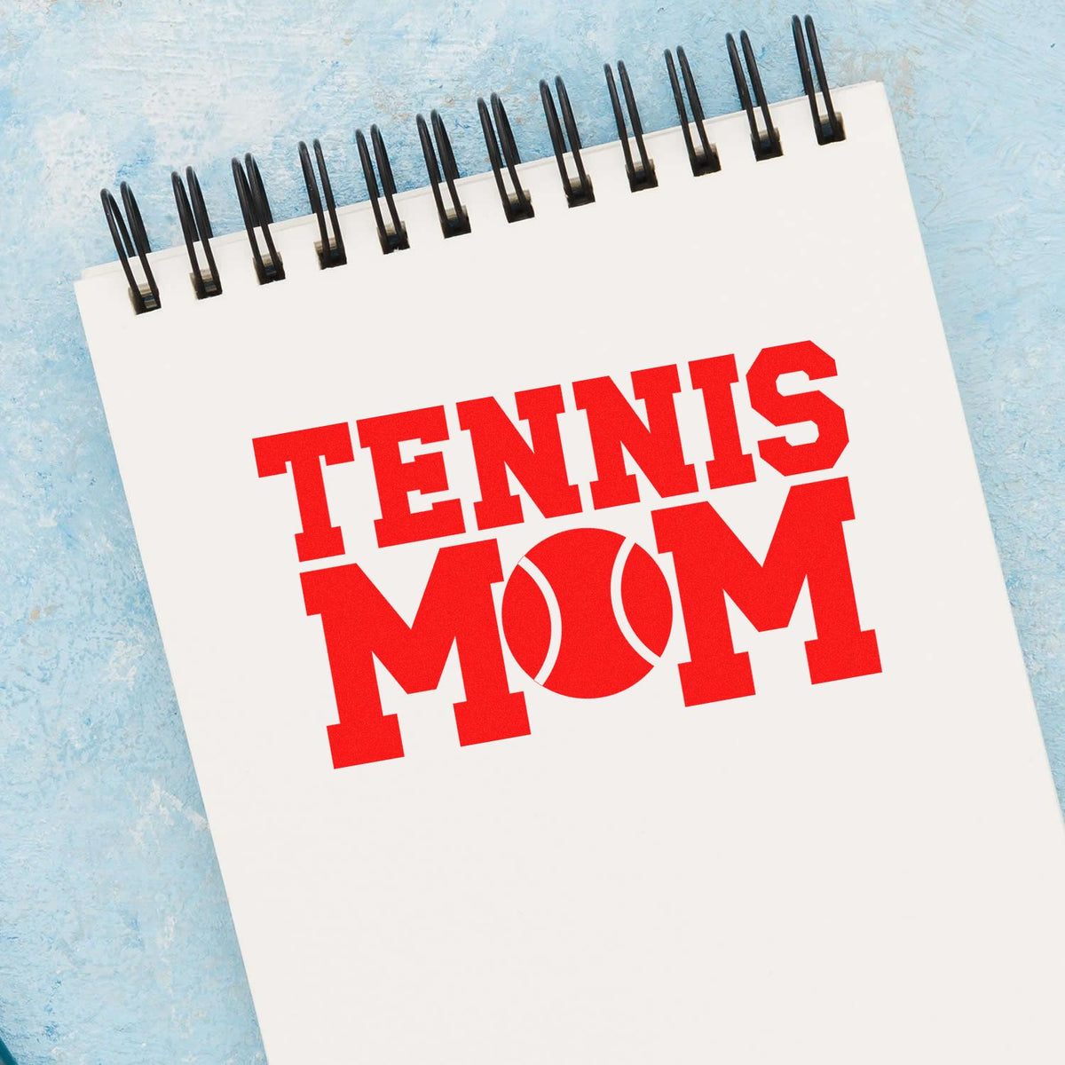 Custom Tennis Mom rubber stamp design on spiral notebook, featuring bold red lettering and a tennis ball graphic.
