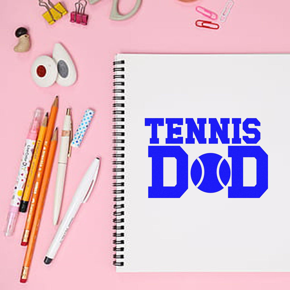Tennis Dad rubber stamp design on a notebook, bold blue sports-themed text for custom gifts, cards and crafts.