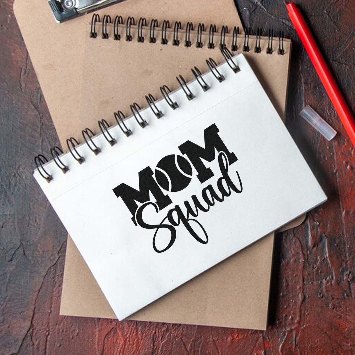 Custom rubber stamp design for Mom Squad, shown on a spiral notebook cover for personalized stationery and craft branding