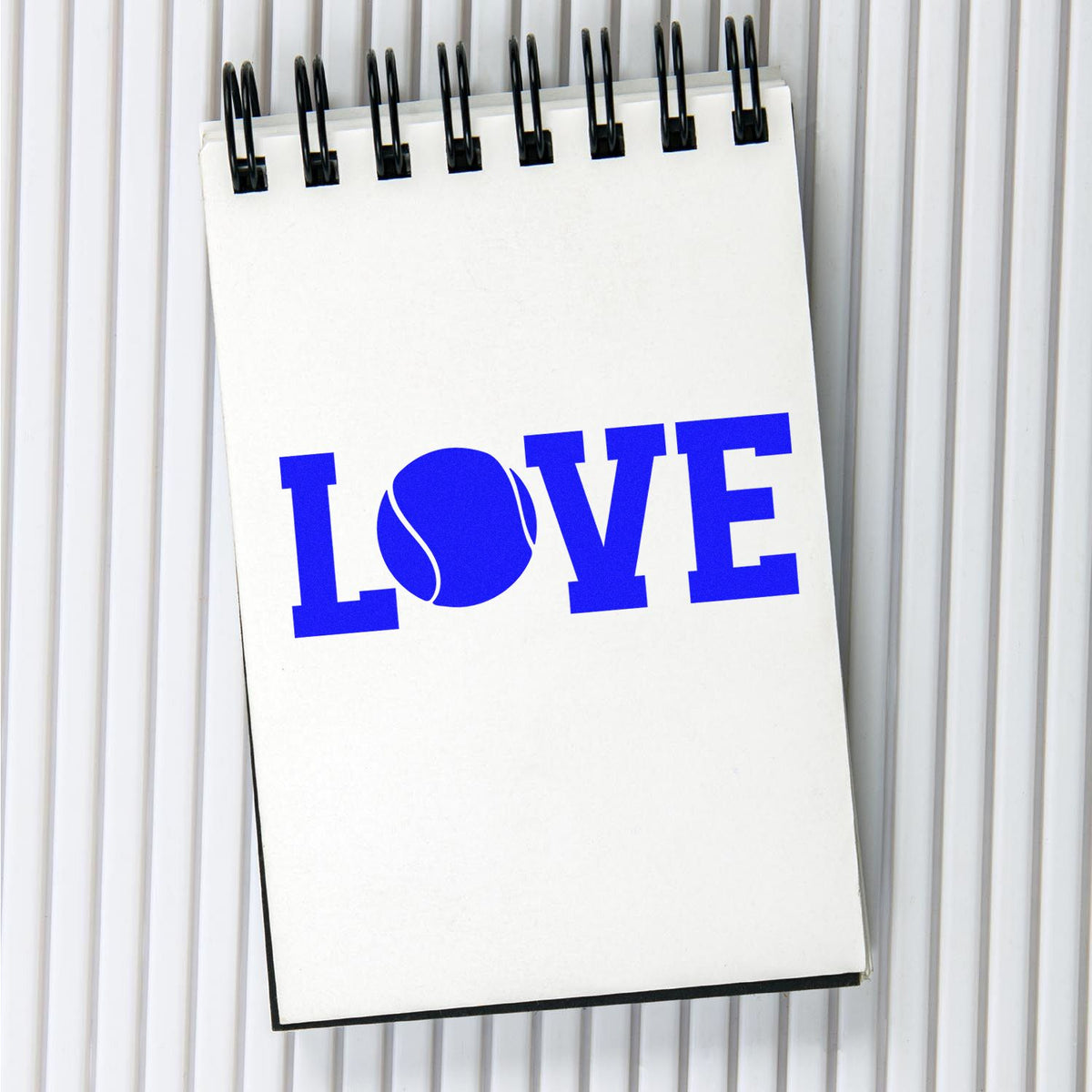 Blue LOVE tennis ball graphic on spiral notebook, perfect for custom rubber stamps.