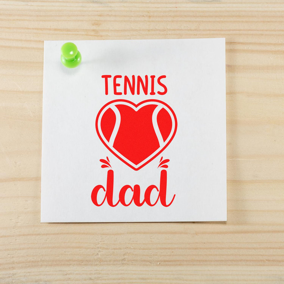 Tennis dad rubber stamp design with heart-shaped tennis ball graphic on a white card pinned to a wood background.