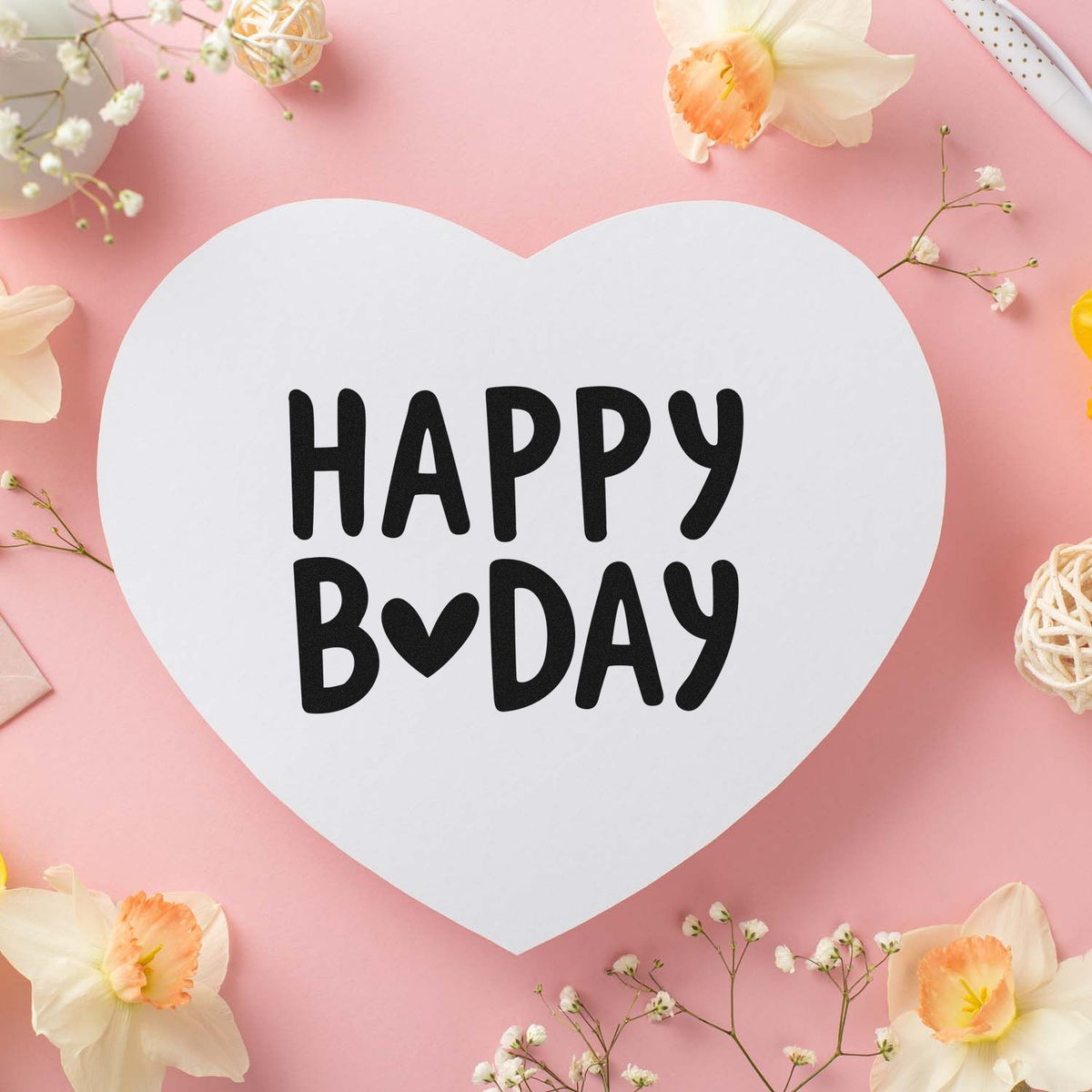 Happy Birthday rubber stamp design with bold black lettering on a heart-shaped card, styled with soft pink floral accents.