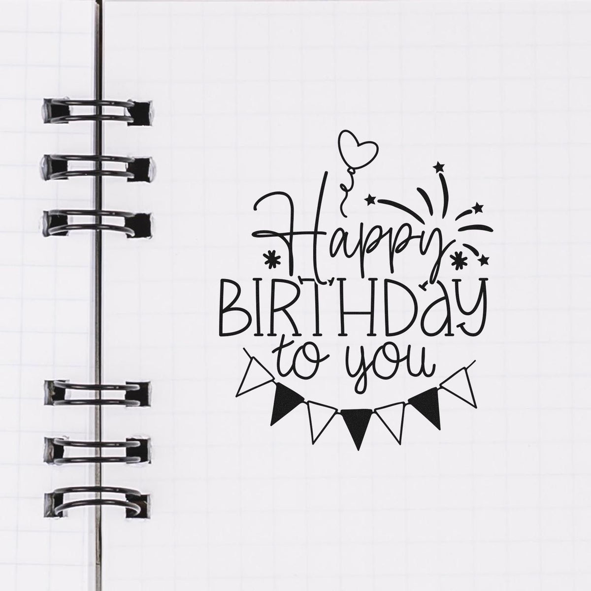 Happy Birthday to You rubber stamp design in a planner notebook, featuring a balloon, bunting, and fireworks accents.