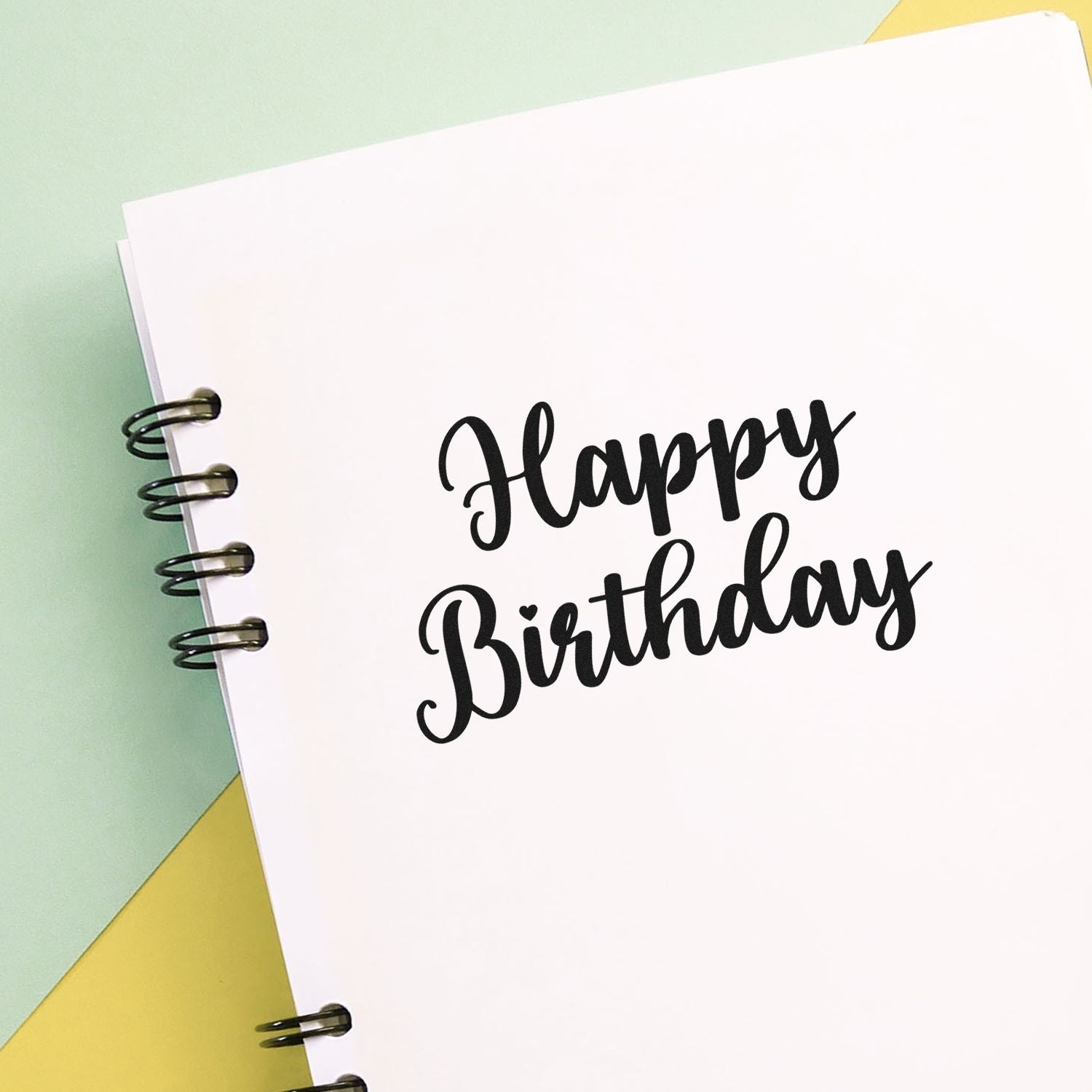 Happy Birthday rubber stamp in bold script on a spiral notebook page, perfect for handmade birthday cards and craft projects.