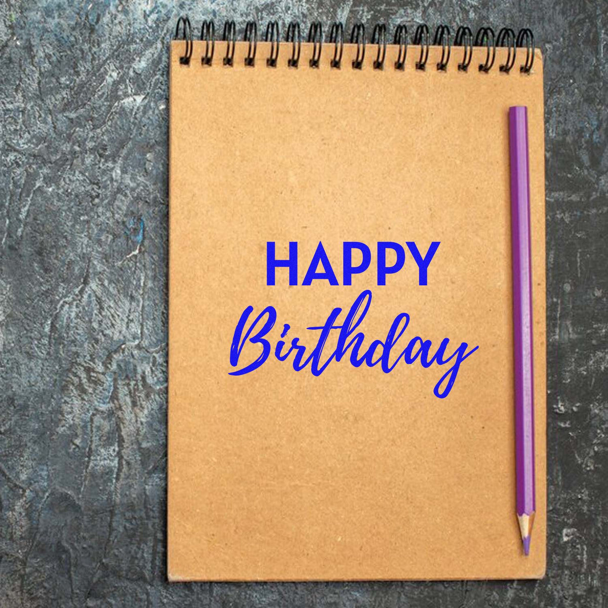 Happy Birthday rubber stamp design in blue on a kraft notebook with pencil, ideal for handmade cards and scrapbook pages.