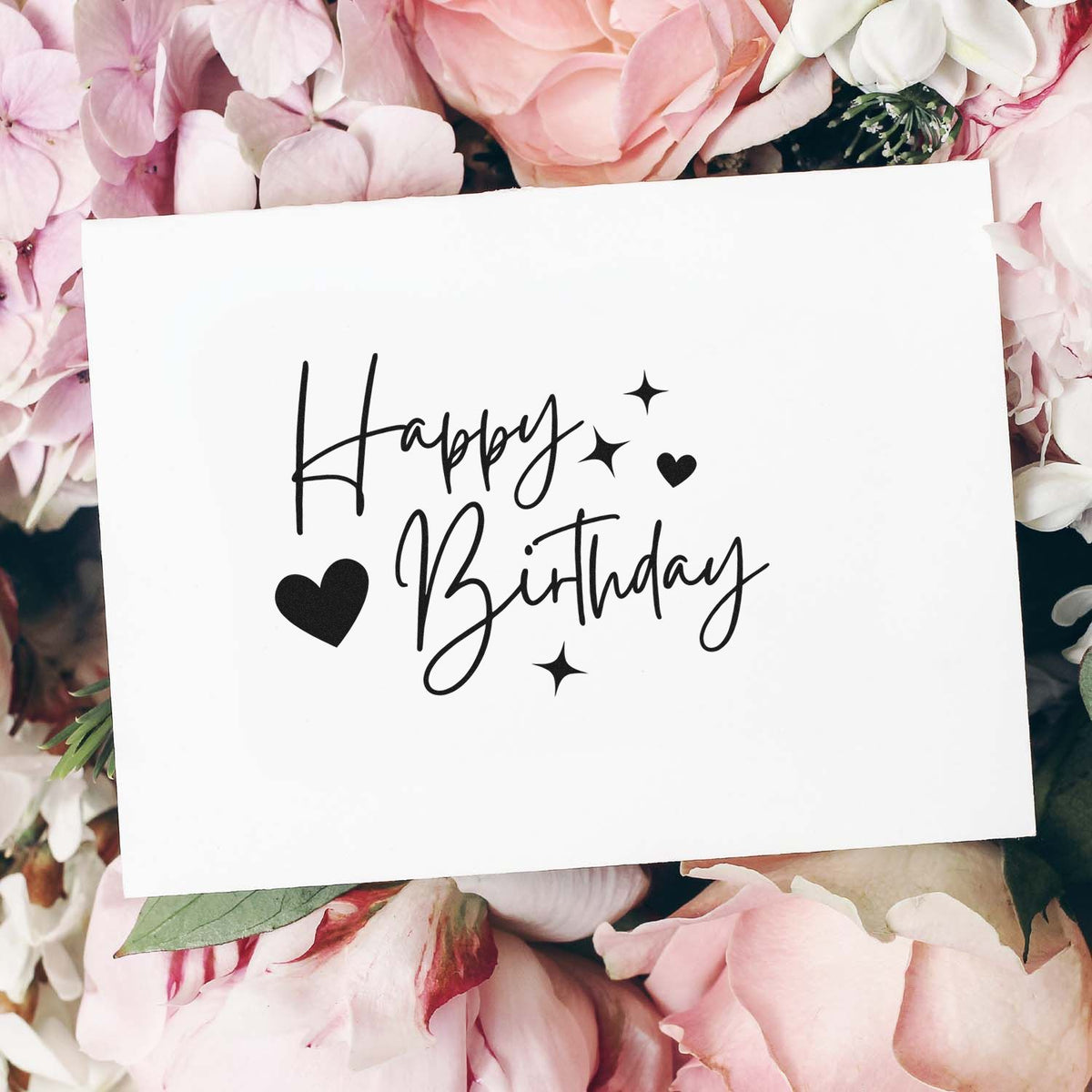 Happy Birthday rubber stamp design with script lettering, hearts and stars on a floral paper card mockup