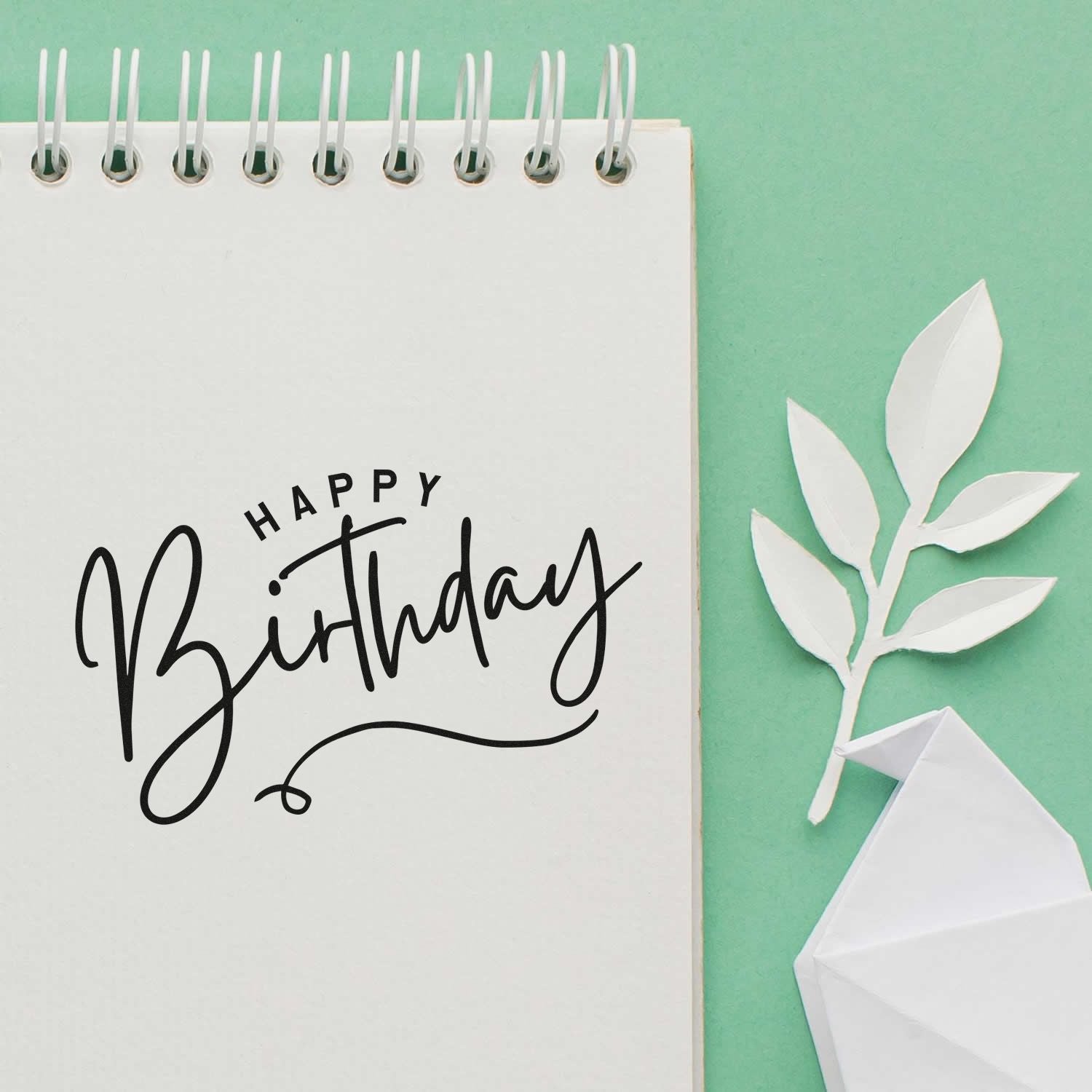 Happy Birthday rubber stamp impression on notebook page with paper craft leaves and origami bird, ideal for handmade cards.