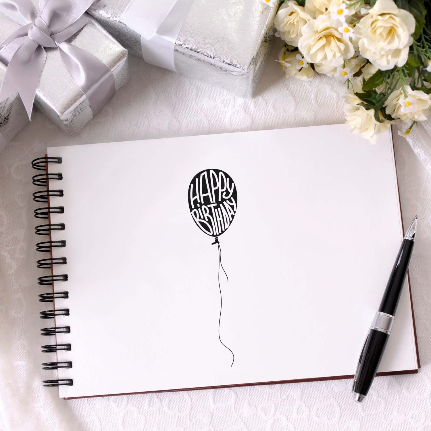 Happy Birthday balloon rubber stamp on blank notebook page for custom birthday card making, with gift boxes and flowers.
