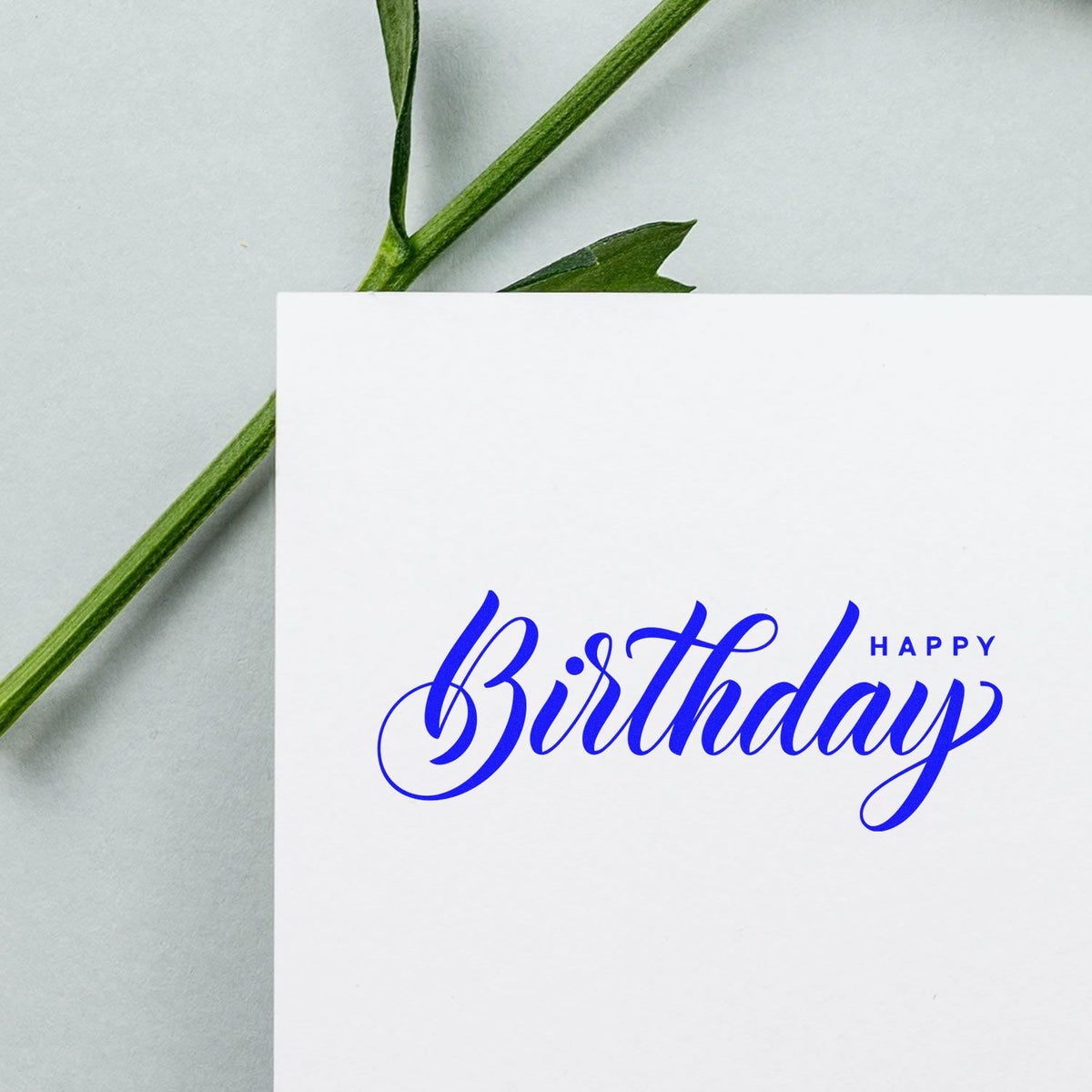 Happy Birthday rubber stamp on white card with blue calligraphy, ideal for custom birthday card making and DIY crafts