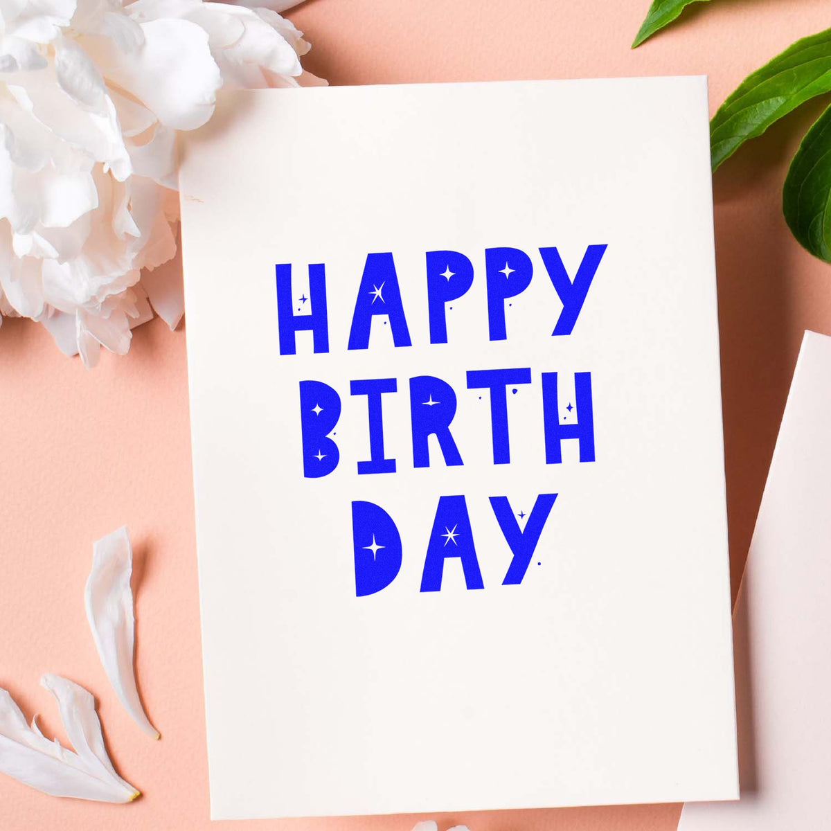 Happy Birthday rubber stamp design in bold blue lettering on a white card with floral accents.