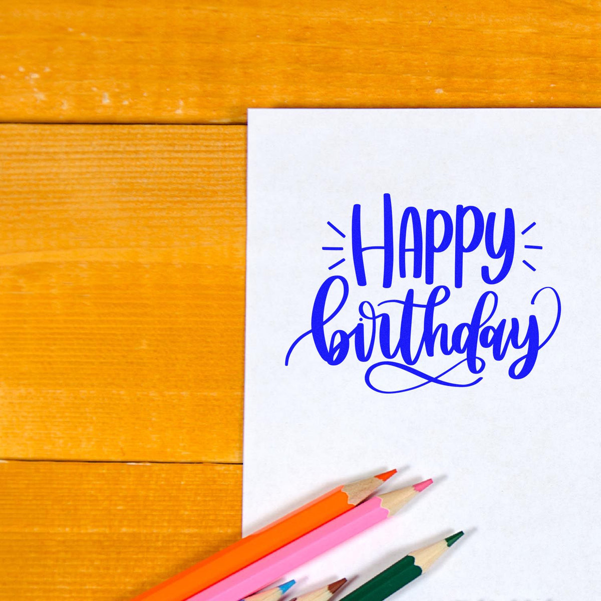 Happy birthday rubber stamp design on white card with colored pencils on a wooden table