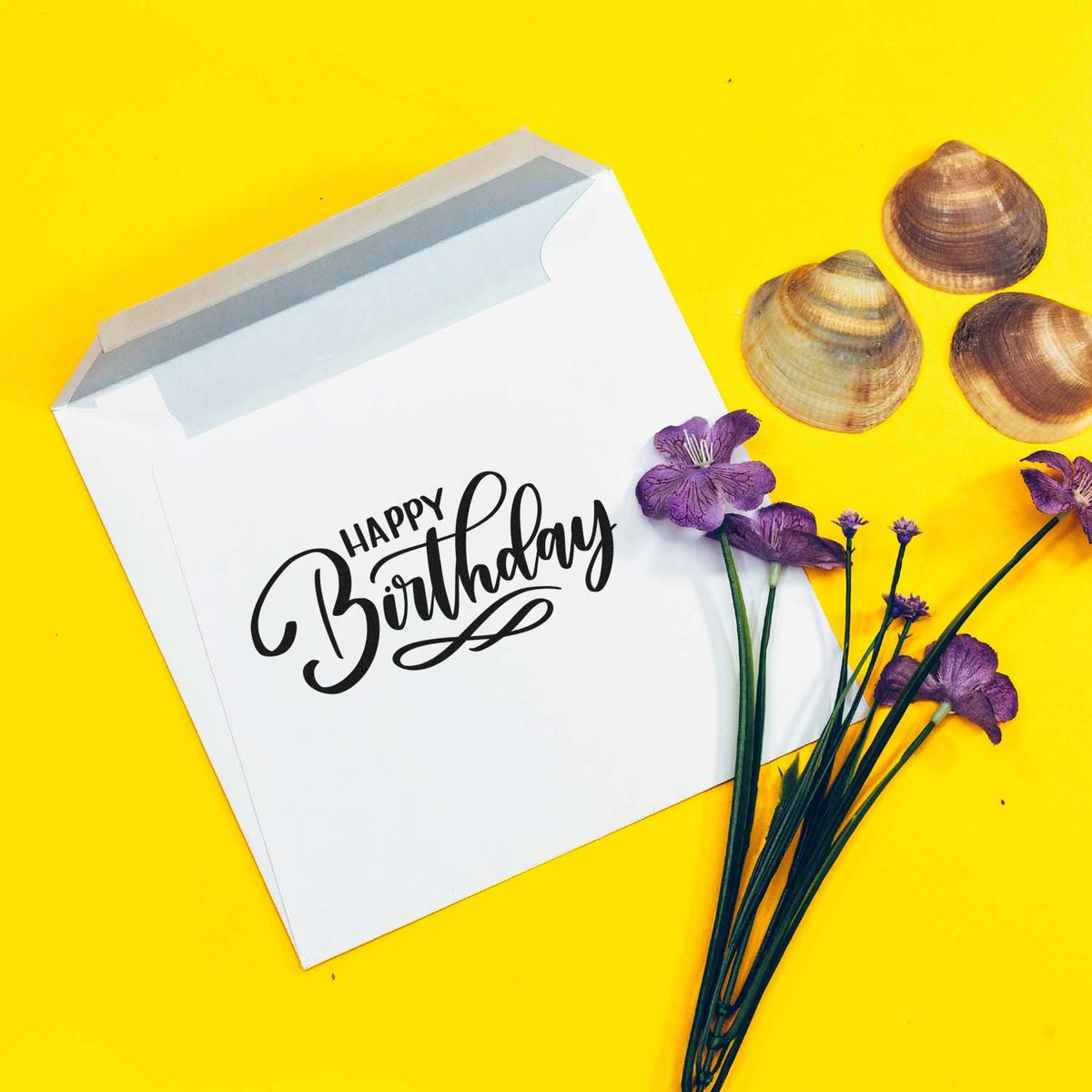 Happy Birthday rubber stamp design on white envelope with purple flowers and seashells, perfect for handmade birthday cards.