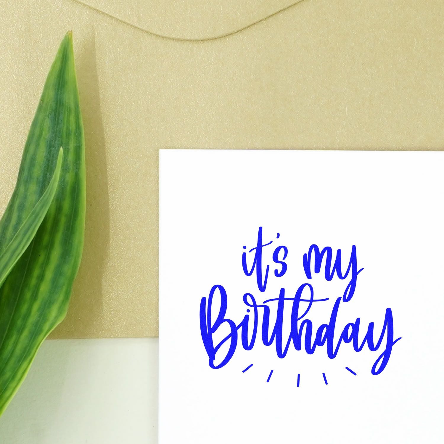 Birthday rubber stamp design with blue script its my Birthday on a white card, styled with green leaf and gold background.