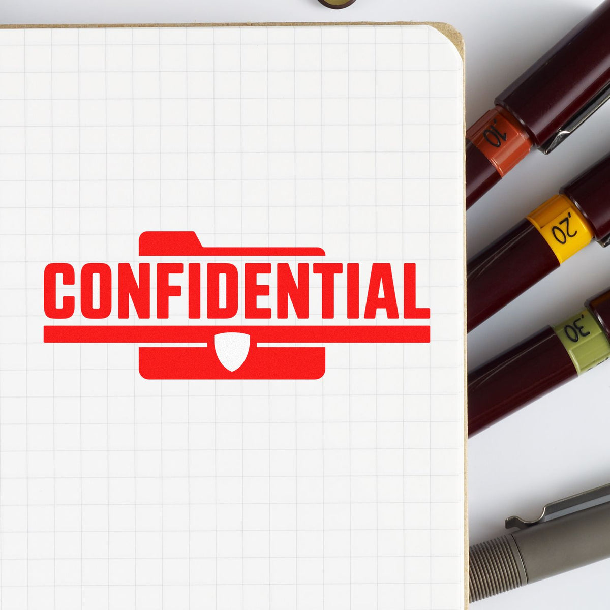 Red confidential rubber stamp on notebook page beside marker pens, used for sensitive document labeling.