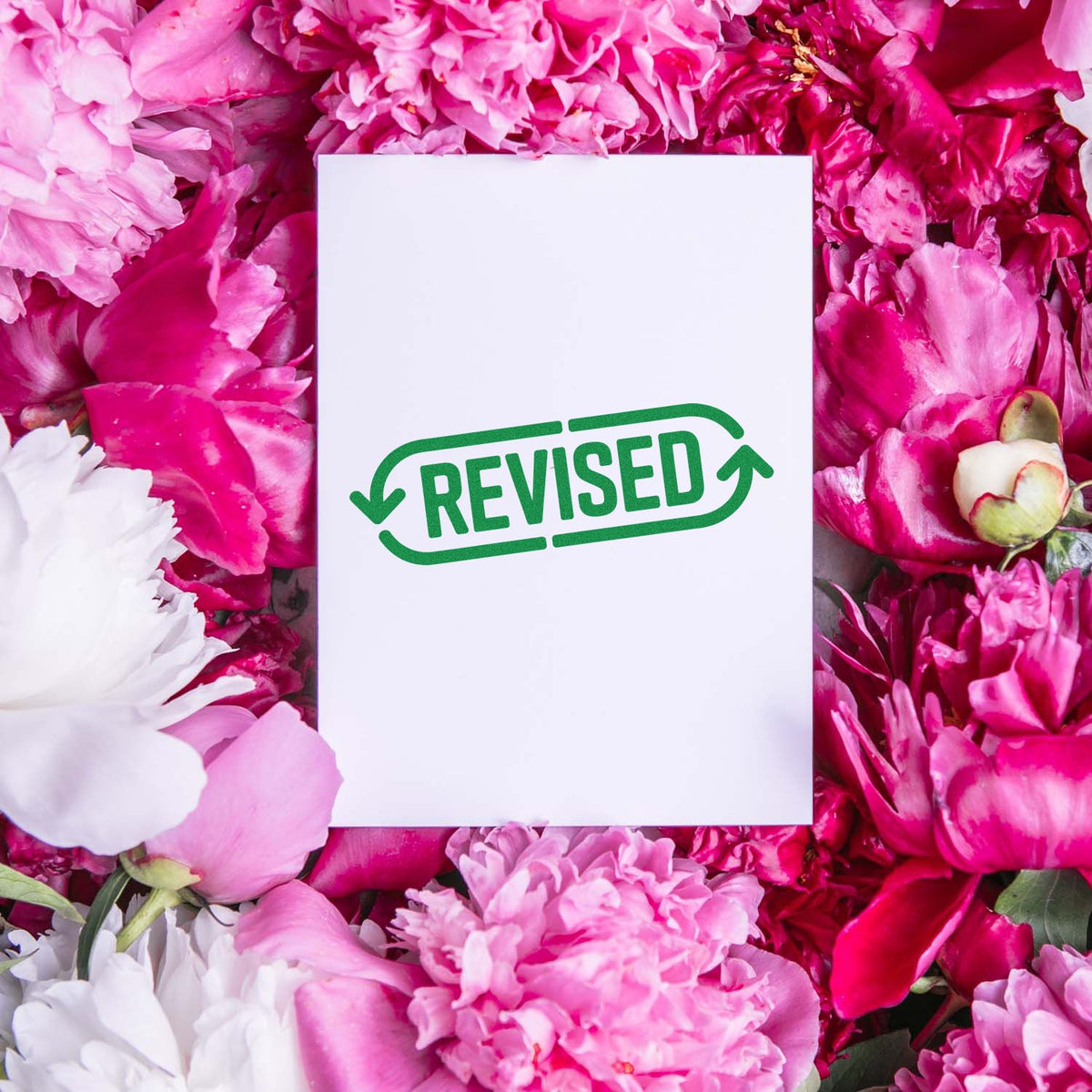 Revised rubber stamp impression on white paper, surrounded by pink flowers.