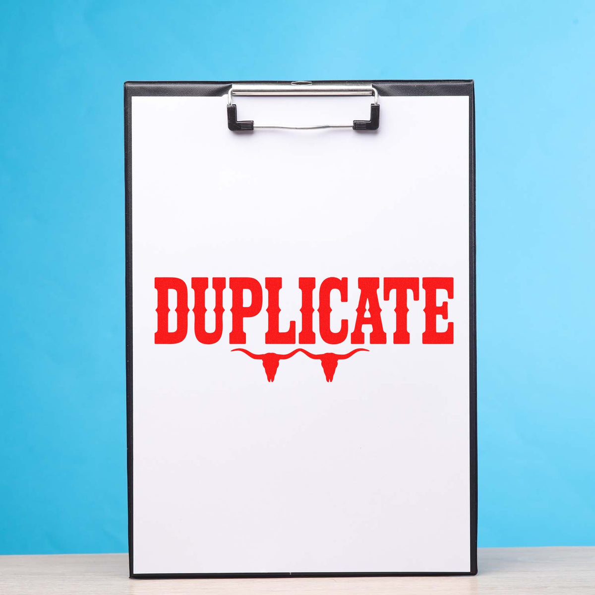 Red duplicate rubber stamp imprint on clipboard for marking office documents.