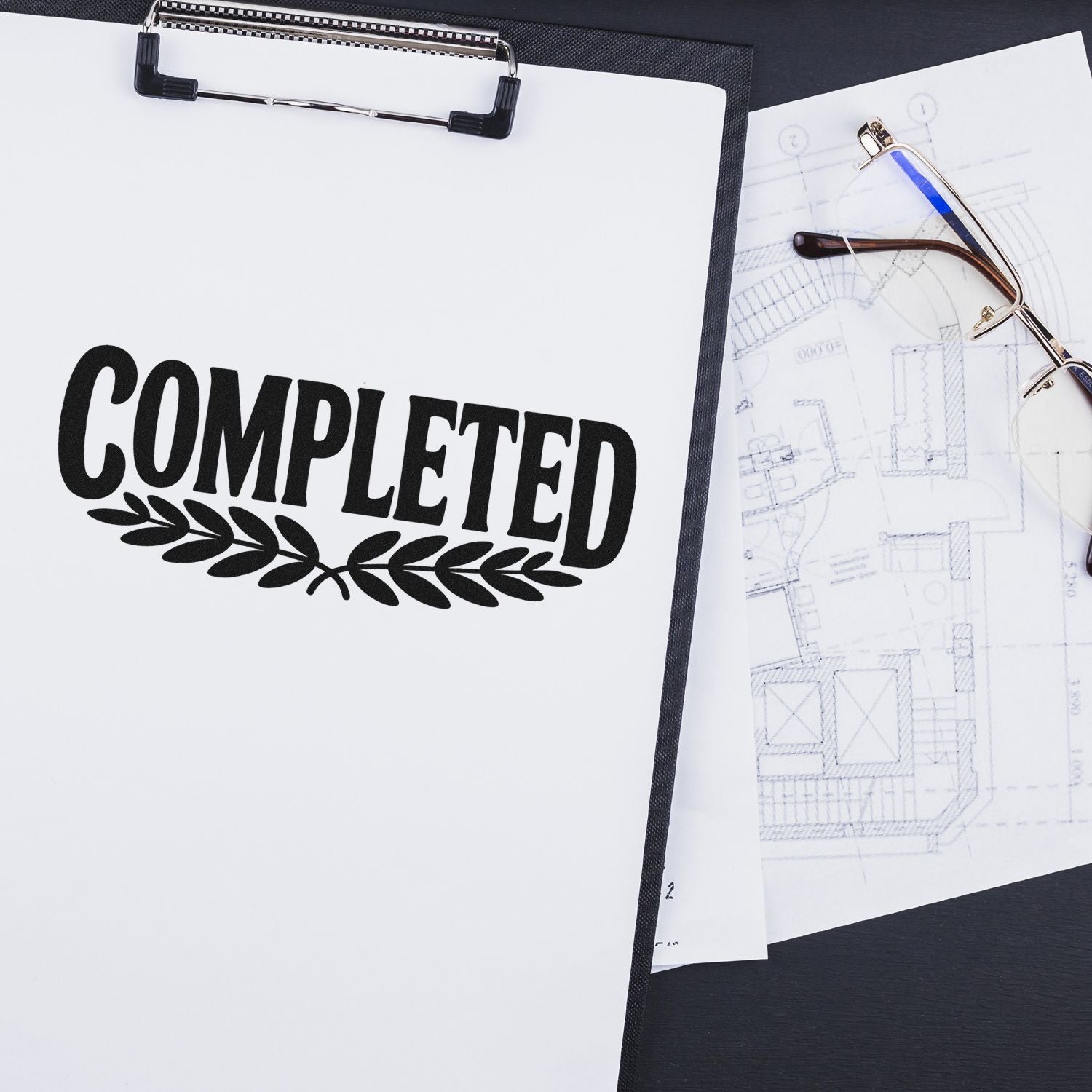 Completed rubber stamp on clipboard with architectural plans and eyeglasses, perfect for document approval and office use.