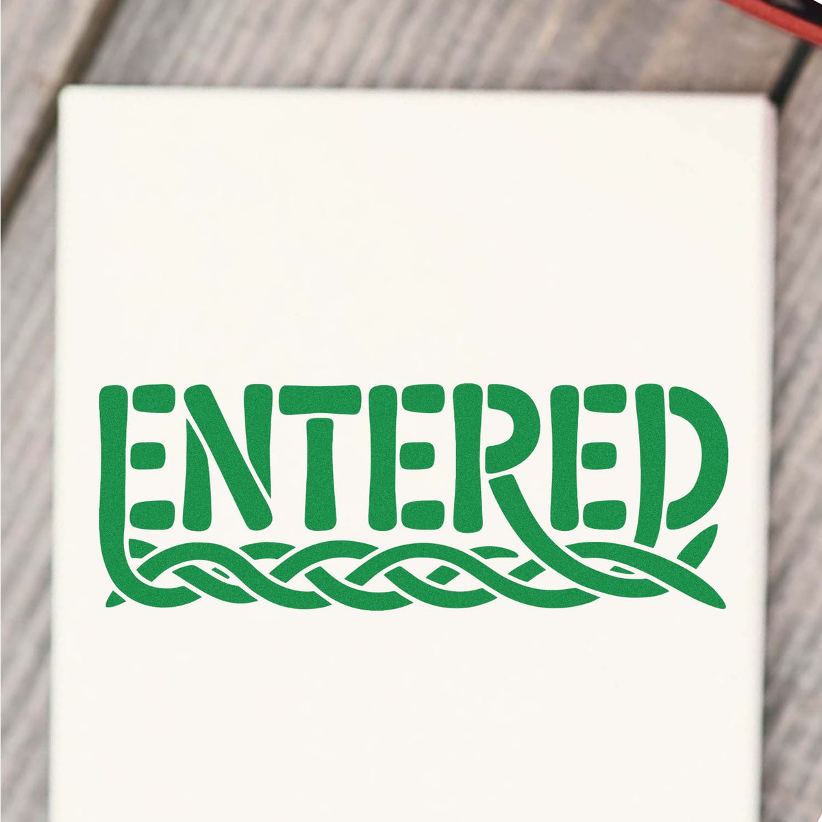 Custom rubber stamp reading ENTERED with decorative woven underline for document approval or filing.