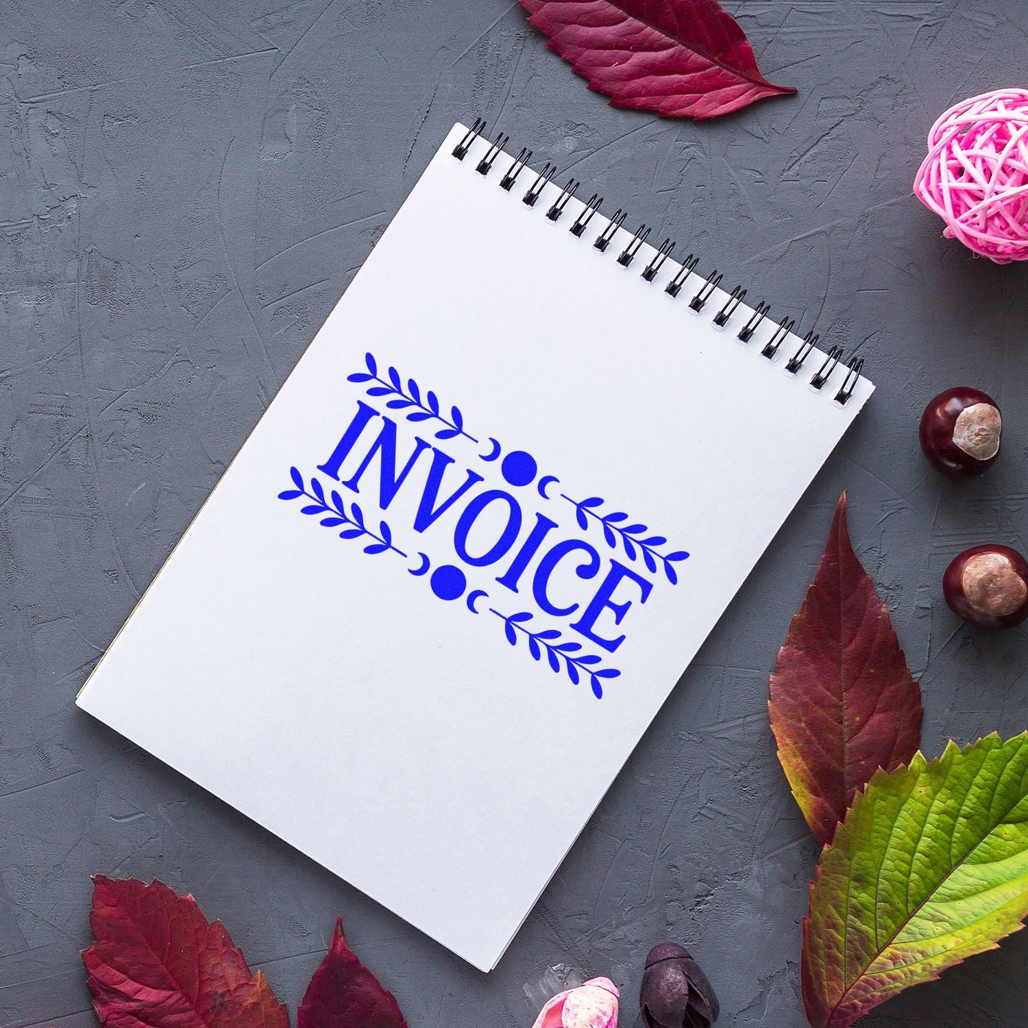 Invoice rubber stamp with decorative leaf border on a spiral notebook, ideal for business paperwork and custom branding.
