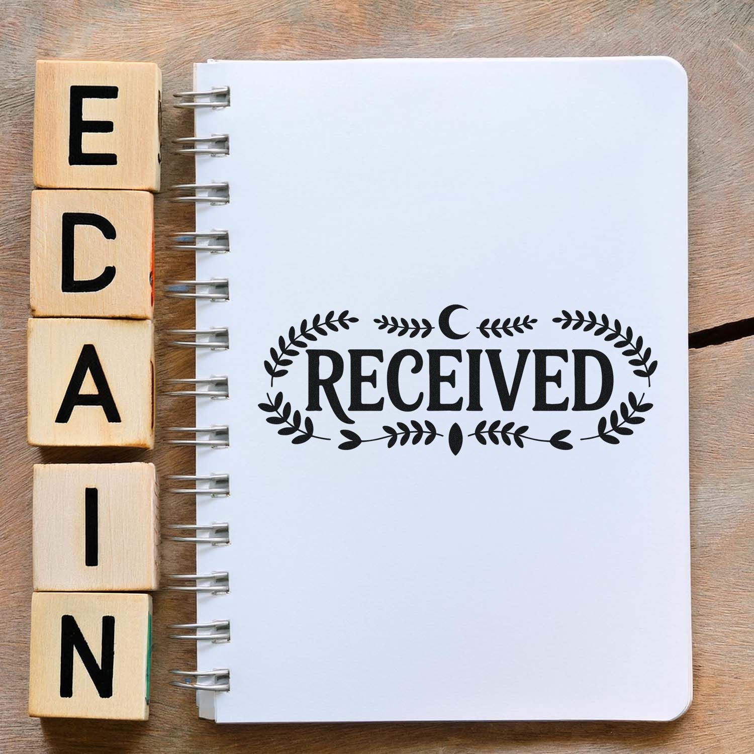 Decorative RECEIVED rubber stamp on a blank notebook, with wooden letter blocks, ideal for office paperwork and craft projects.