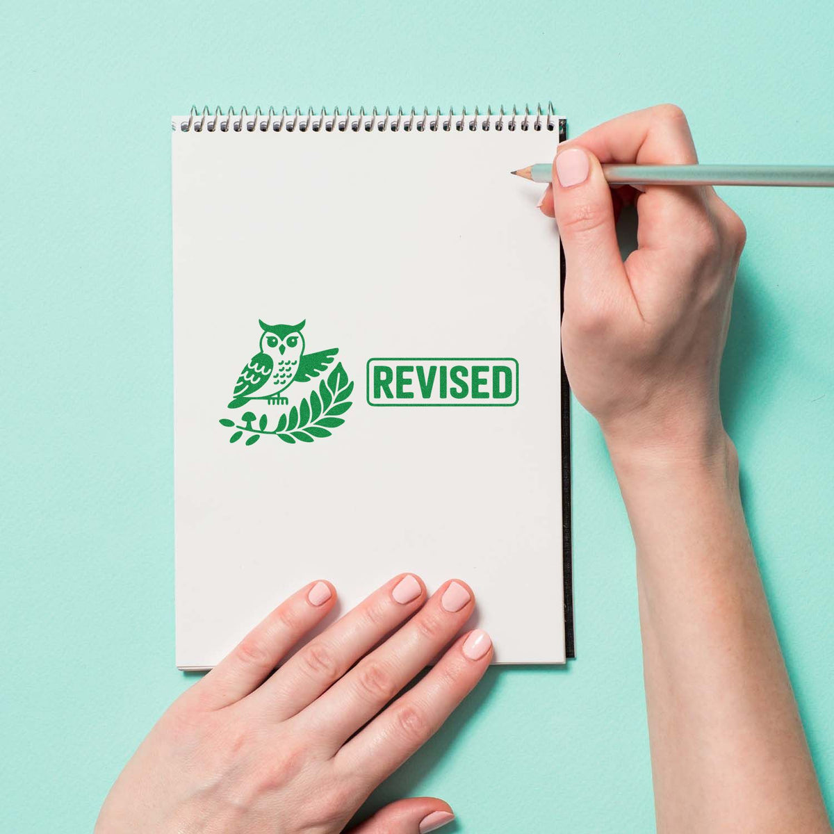 Green revised rubber stamp with owl icon on notebook page, used for proofreading and document editing.