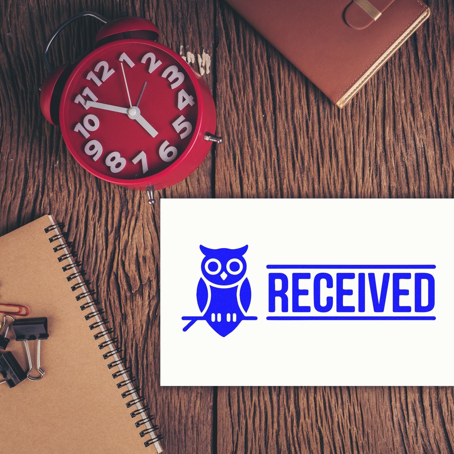 Received rubber stamp design with owl icon for office paperwork, shown on a desk with clock and notebook.