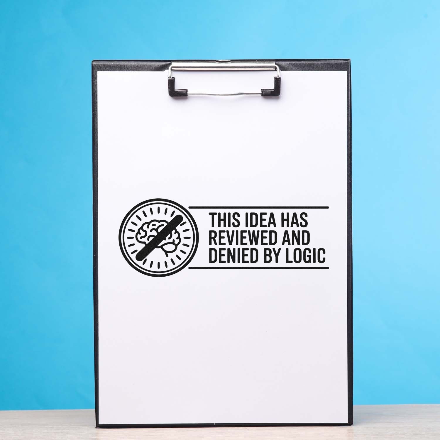 Funny rubber stamp design on clipboard: "This idea has been reviewed and denied by logic" for office approval rejection.