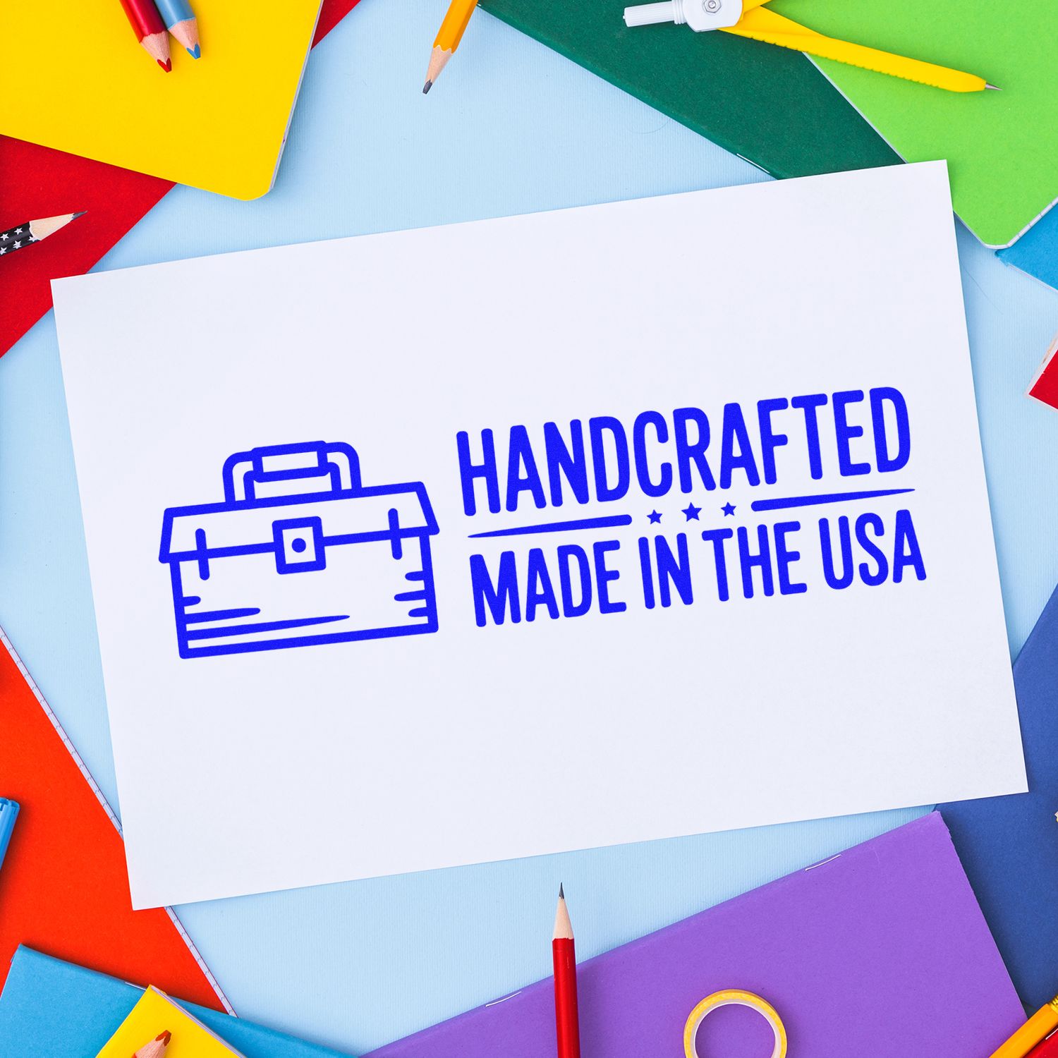 Handcrafted Made in the USA rubber stamp impression on paper, surrounded by colorful stationery supplies.