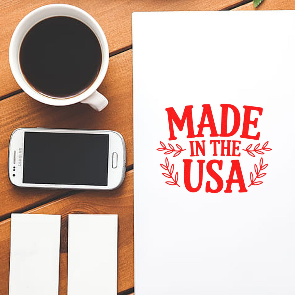 Made in the USA rubber stamp design mockup on white paper with coffee cup and smartphone on a wooden desk.