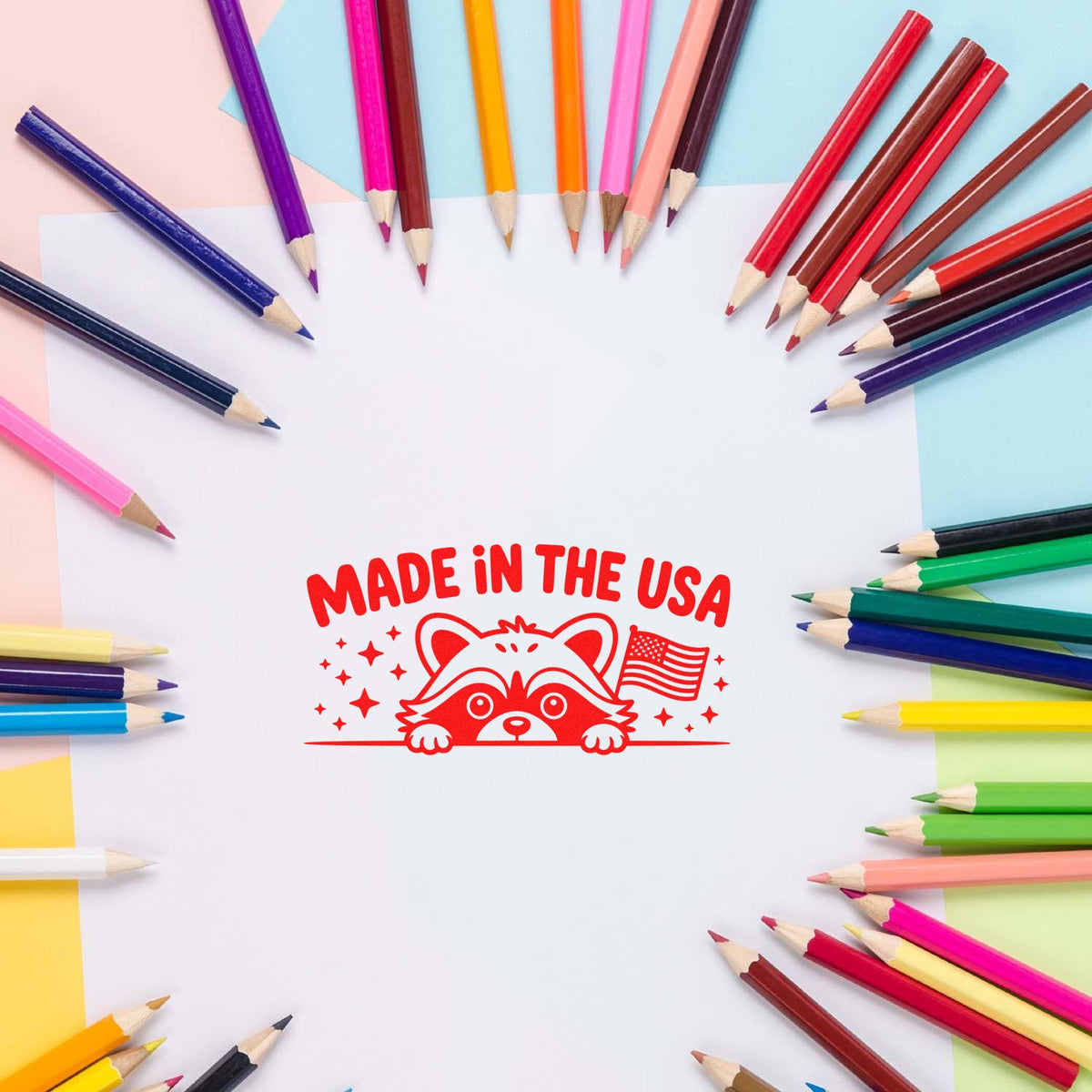Made in USA raccoon rubber stamp design on white paper, surrounded by colored pencils for custom craft and packaging branding.