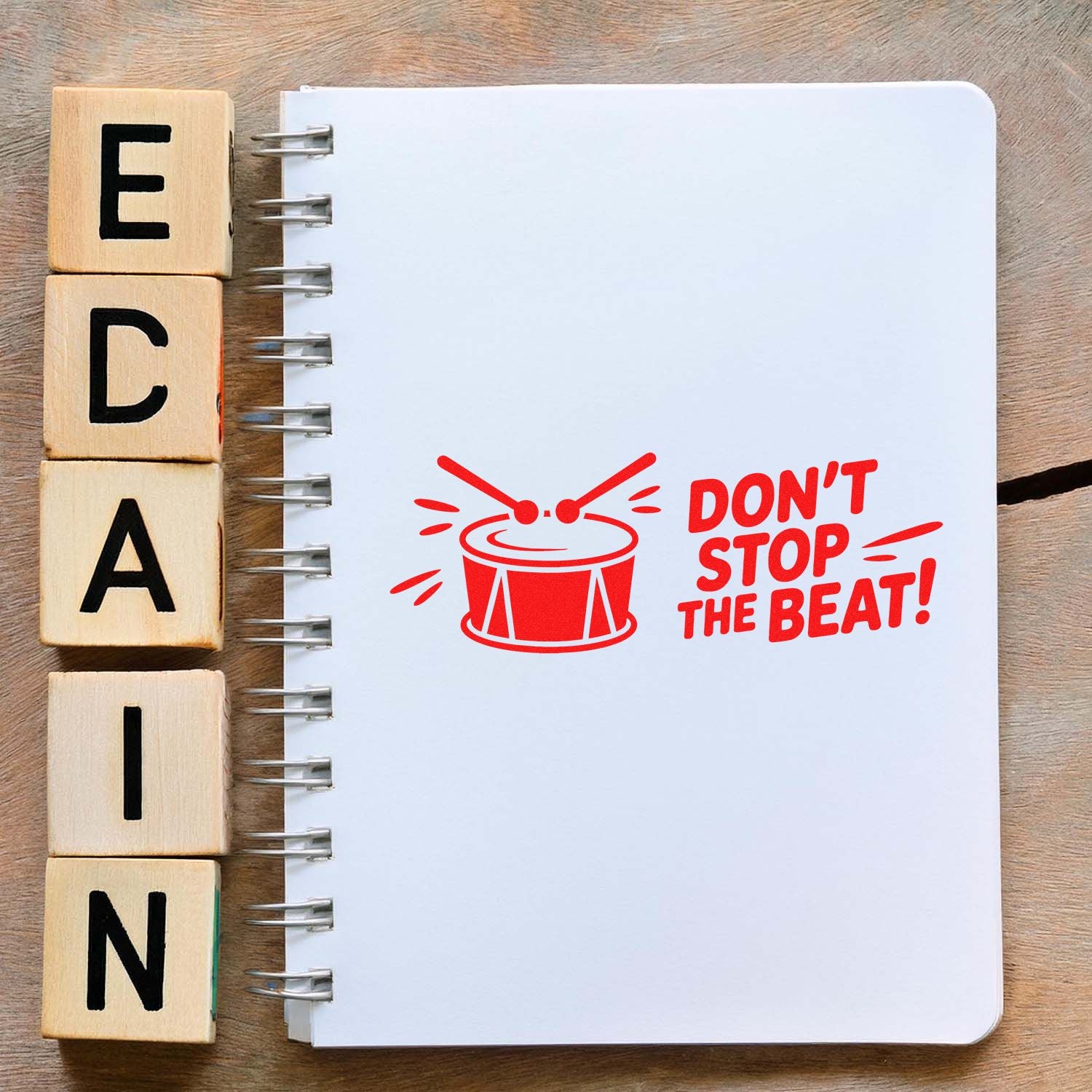 Wooden letter blocks beside a notebook featuring a red drum rubber stamp reading Dont Stop the Beat! for music-themed crafts.