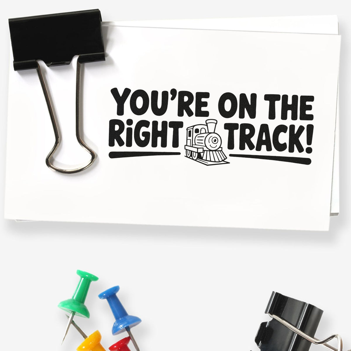 Custom rubber stamp reading Youre on the right track! with train icon on white paper clip display.