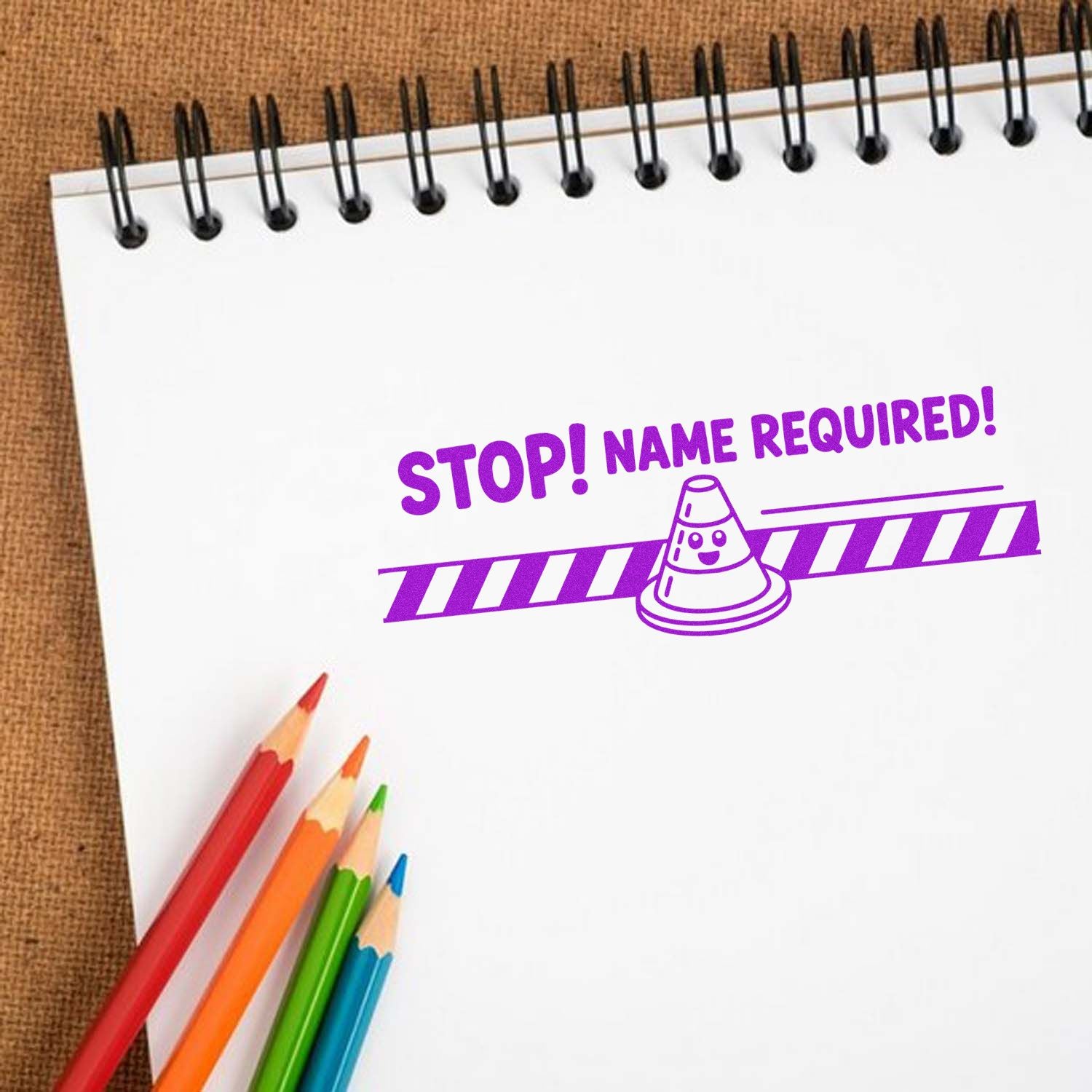 Custom rubber stamp design reading "STOP! NAME REQUIRED!" on notebook paper with colored pencils.