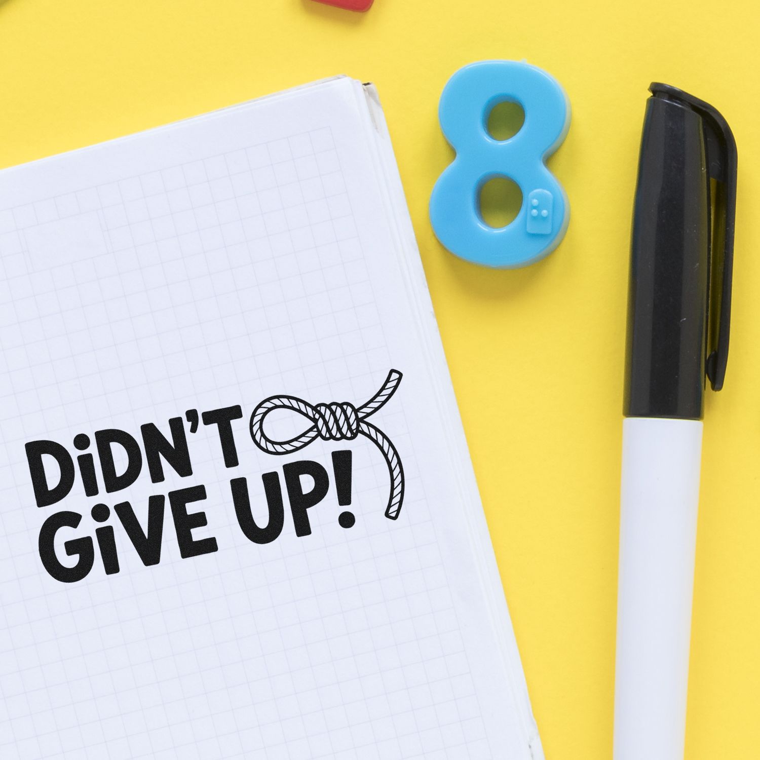 Custom rubber stamp concept with Didnt Give Up! message on notebook, shown with pen and number 8 stamp on yellow background.
