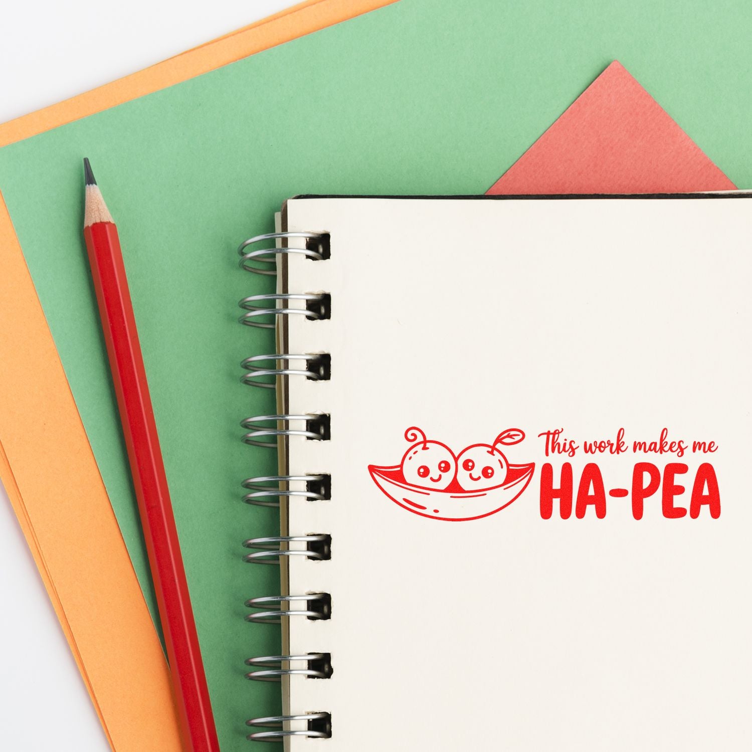 Rubber stamp design with This work makes me HA-PEA pea pun on notebook page, with red pencil and colorful paper background.