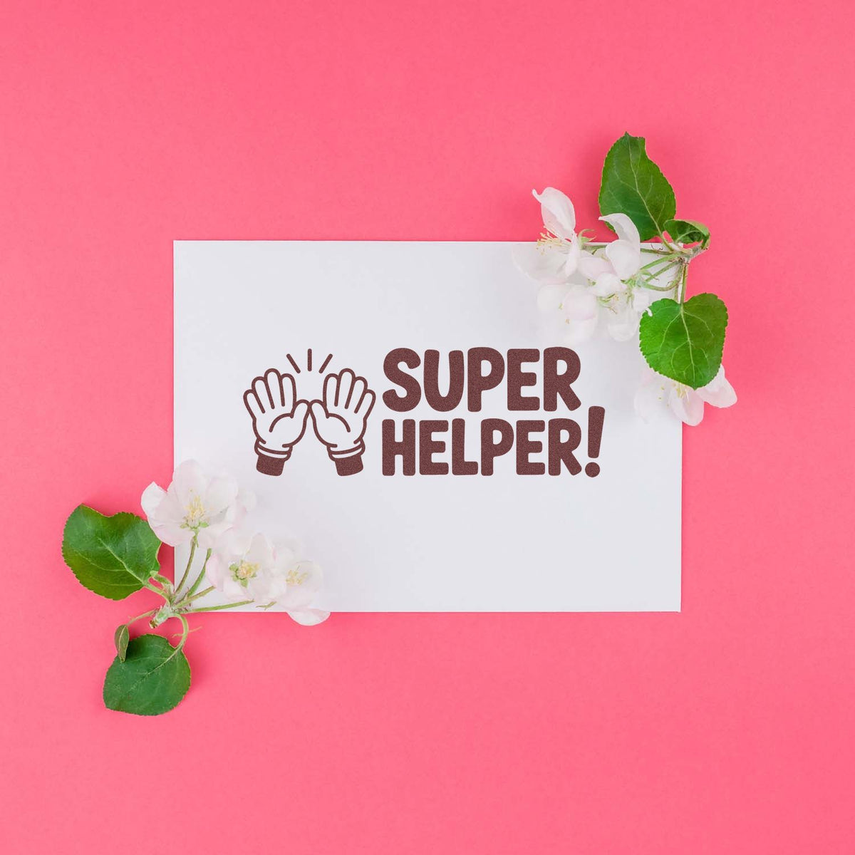 Super Helper rubber stamp with clapping hands icon, shown on a white card with flowers on a pink background.