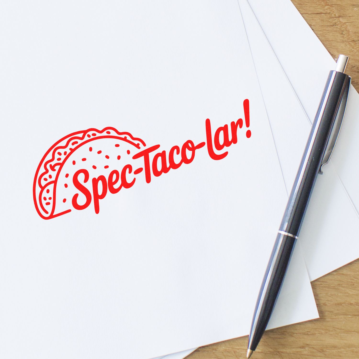 Custom rubber stamp with red Spec-Taco-lar! taco design on paper beside pen