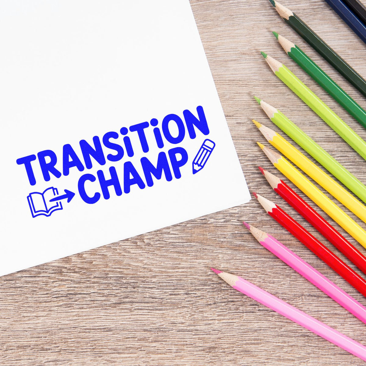 Blue custom rubber stamp reading Transition Champ on paper, with colored pencils on a wooden desk.